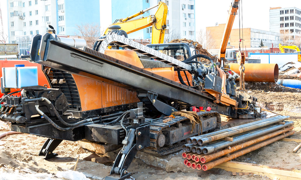 Orange horizontal directional drilling machine with drill rods on construction site for trenchless installation